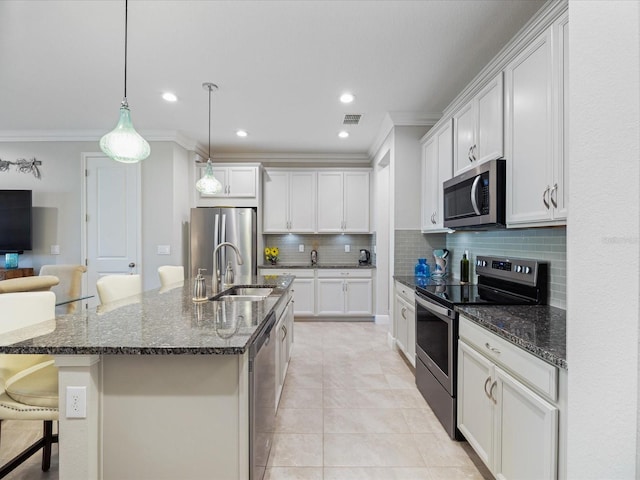 kitchen with a breakfast bar, dark stone countertops, stainless steel appliances, an island with sink, and white cabinets