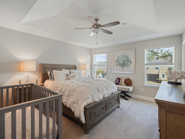 bedroom with ceiling fan, light colored carpet, a raised ceiling, and multiple windows