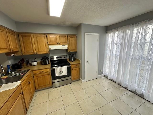 kitchen with light tile patterned flooring, sink, a textured ceiling, and stainless steel electric range