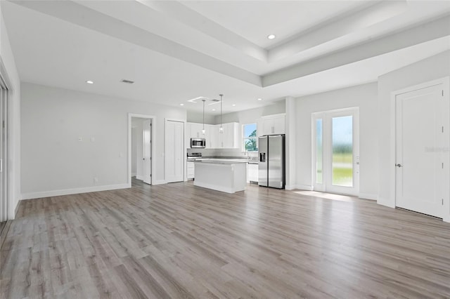 unfurnished living room with a raised ceiling, sink, and light hardwood / wood-style flooring