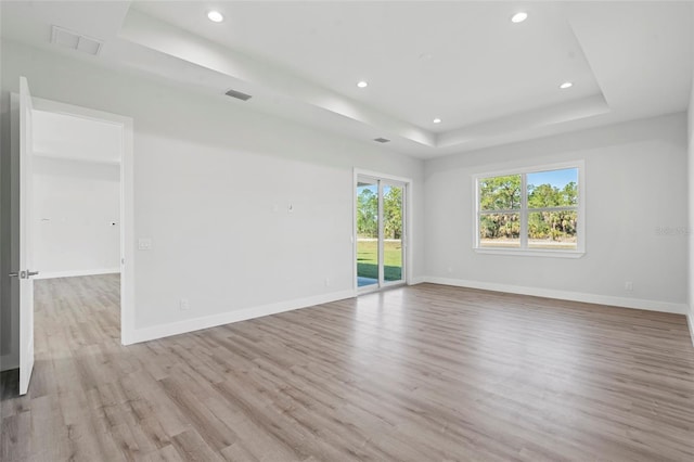 empty room featuring a raised ceiling and light hardwood / wood-style flooring