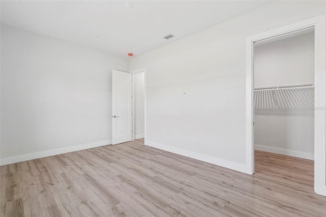 unfurnished bedroom featuring a walk in closet, light hardwood / wood-style floors, and a closet