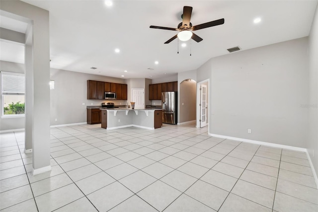 kitchen featuring a kitchen island with sink, light tile patterned floors, stainless steel appliances, and a kitchen bar