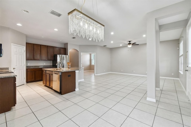 kitchen with light tile patterned flooring, stainless steel appliances, sink, and a kitchen island with sink