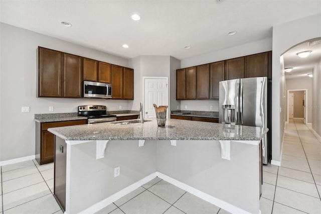 kitchen featuring sink, stainless steel appliances, an island with sink, and light stone countertops