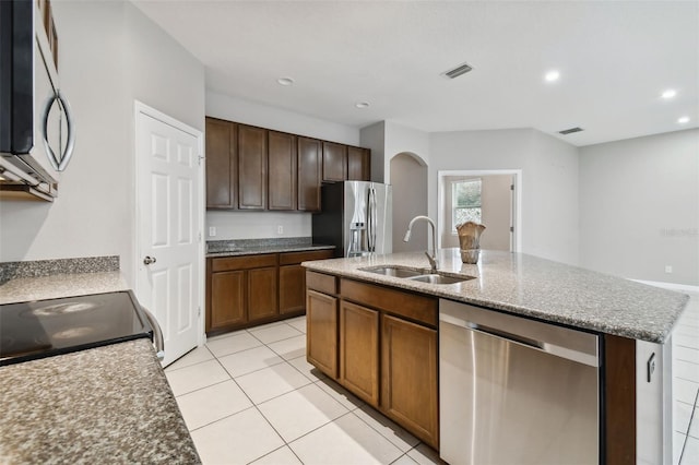 kitchen featuring light tile patterned flooring, appliances with stainless steel finishes, an island with sink, sink, and light stone counters