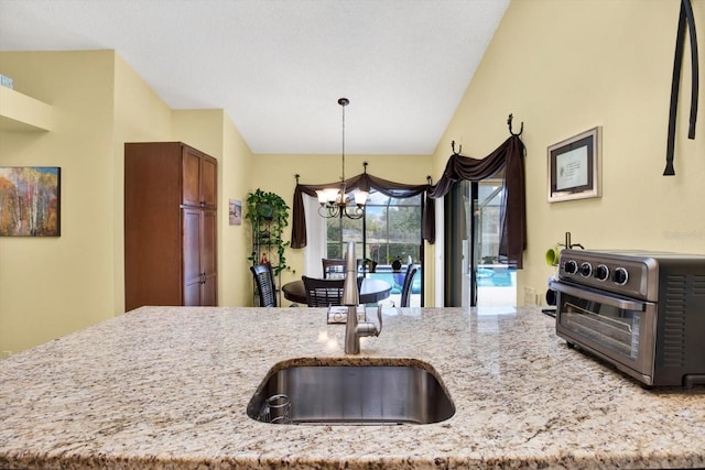 kitchen with pendant lighting, vaulted ceiling, light stone countertops, and a chandelier