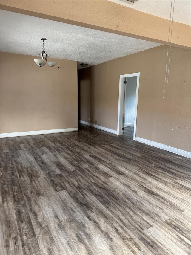 empty room with dark wood-type flooring, a notable chandelier, a textured ceiling, and baseboards