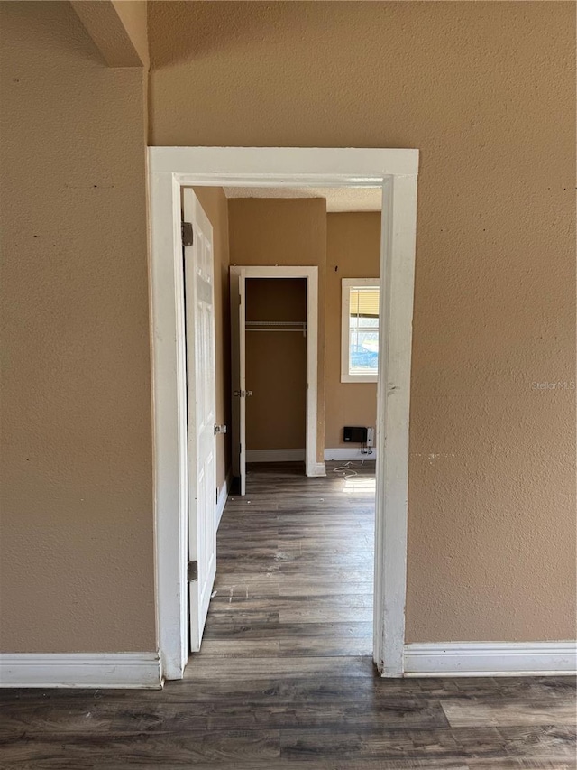 hallway featuring dark wood-type flooring, a textured wall, and baseboards