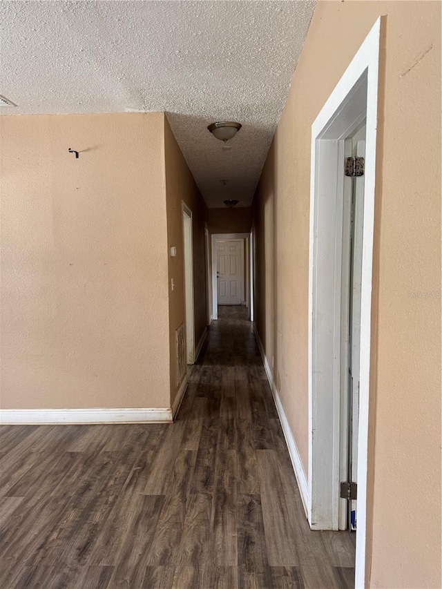 corridor with dark wood-type flooring, visible vents, a textured ceiling, and baseboards