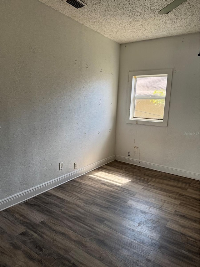 empty room with dark wood finished floors, visible vents, a textured wall, a textured ceiling, and baseboards