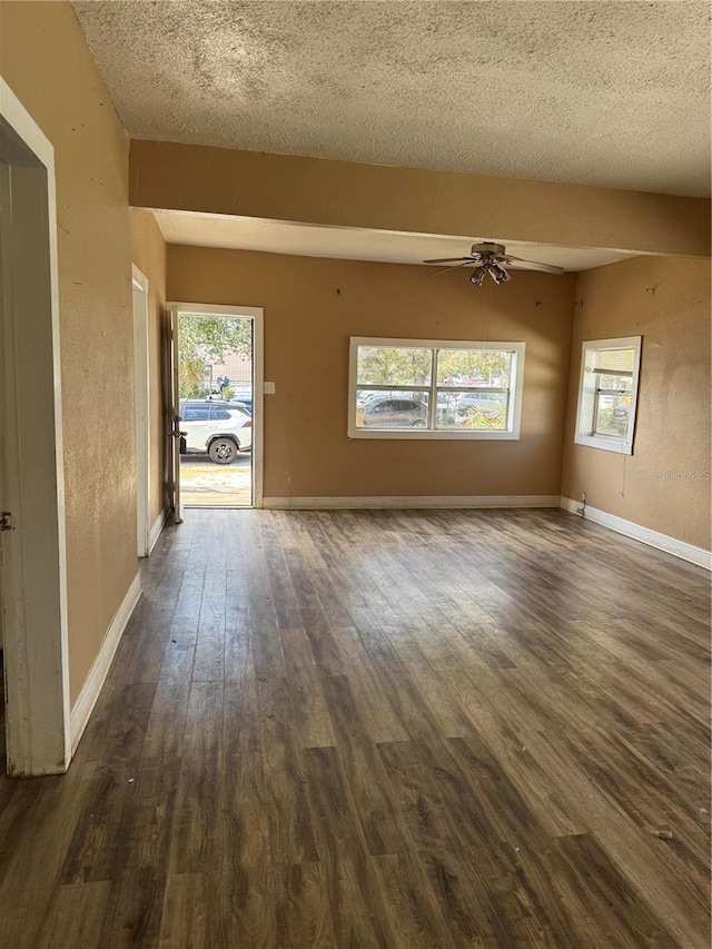 unfurnished living room featuring ceiling fan, a textured ceiling, baseboards, and dark wood-style flooring