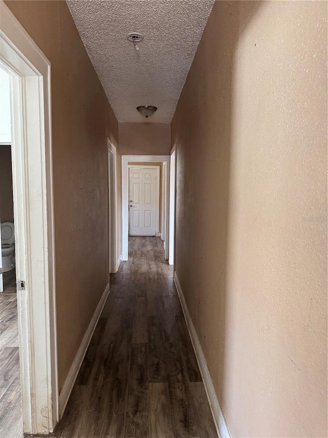 hall with a textured ceiling, baseboards, wood finished floors, and a textured wall