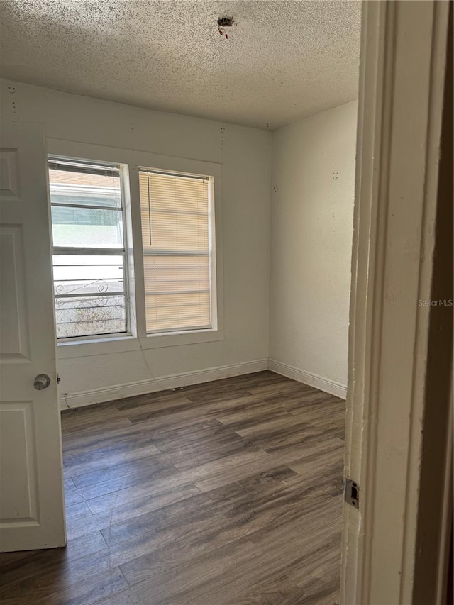 unfurnished room with a textured ceiling, dark wood finished floors, and baseboards