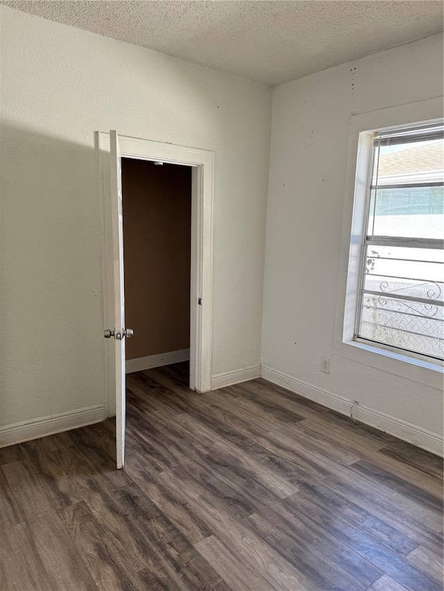 empty room featuring a textured ceiling, baseboards, and dark wood-style flooring