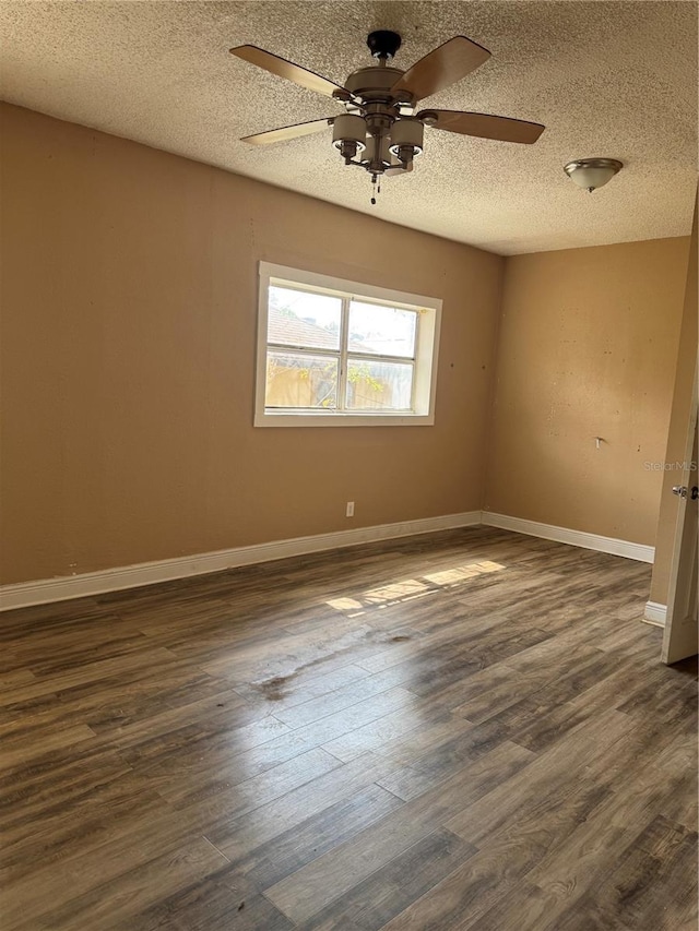 empty room featuring a textured ceiling, dark wood finished floors, and baseboards