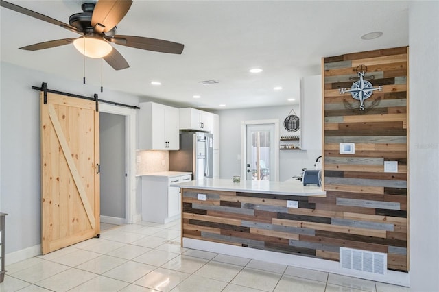 kitchen with stainless steel refrigerator, tasteful backsplash, white cabinetry, light tile patterned floors, and a barn door