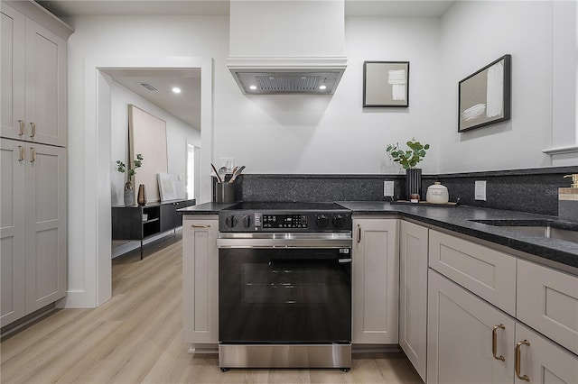 kitchen with premium range hood, sink, dark stone counters, light hardwood / wood-style floors, and stainless steel electric range