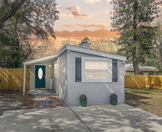 view of front of home featuring fence, a chimney, and stucco siding