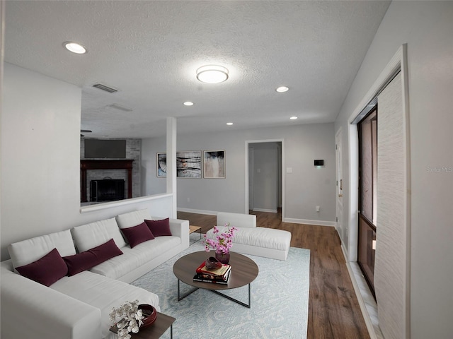 living room featuring hardwood / wood-style flooring, a brick fireplace, and a textured ceiling