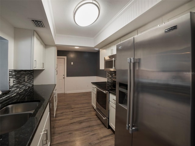 kitchen with dark hardwood / wood-style floors, white cabinetry, dark stone counters, stainless steel appliances, and crown molding