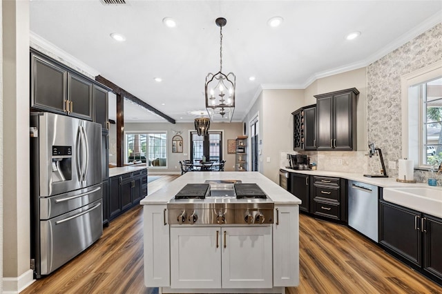 kitchen with dark wood-type flooring, crown molding, appliances with stainless steel finishes, a kitchen island, and pendant lighting