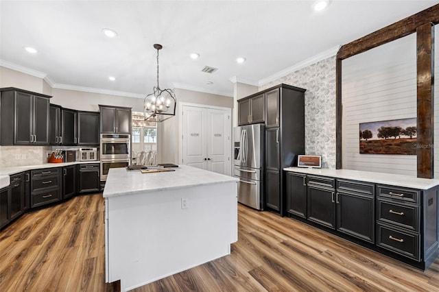 kitchen with a kitchen island, decorative light fixtures, hardwood / wood-style flooring, ornamental molding, and stainless steel appliances