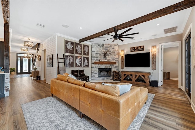 living room with beamed ceiling, ceiling fan with notable chandelier, a large fireplace, and hardwood / wood-style floors