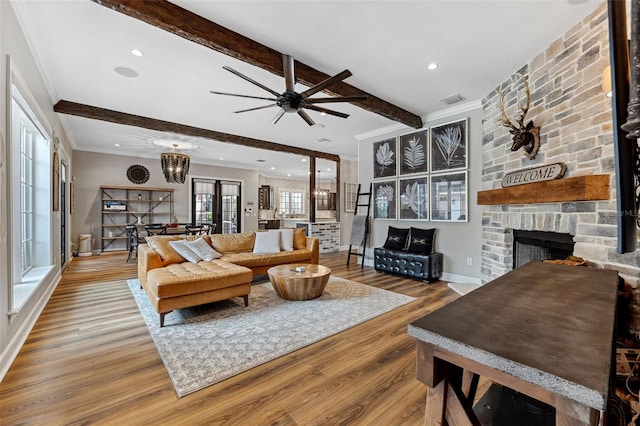 living room with beamed ceiling, wood-type flooring, a stone fireplace, and ornamental molding