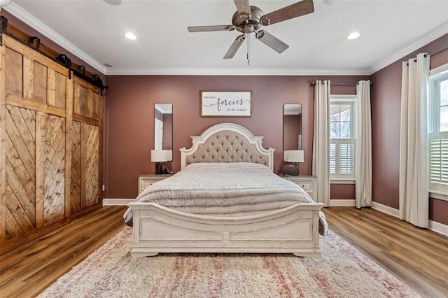 bedroom with crown molding, ceiling fan, a barn door, and hardwood / wood-style floors