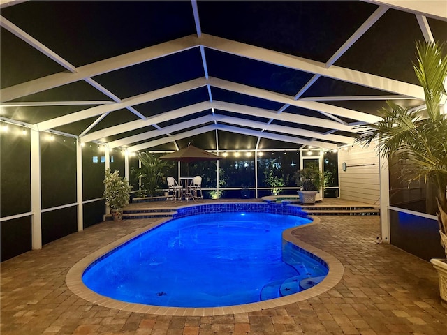 pool at twilight with glass enclosure and a patio area