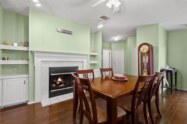 dining room with a tile fireplace, dark wood-type flooring, ceiling fan, and a textured ceiling