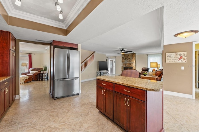 kitchen featuring crown molding, a textured ceiling, stainless steel fridge, a raised ceiling, and a fireplace