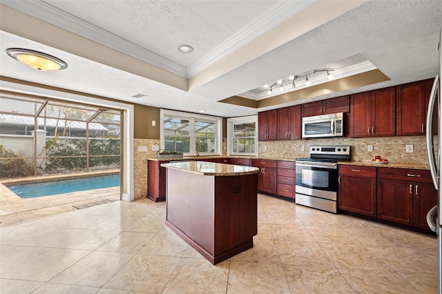 kitchen with appliances with stainless steel finishes, a tray ceiling, a center island, and a textured ceiling