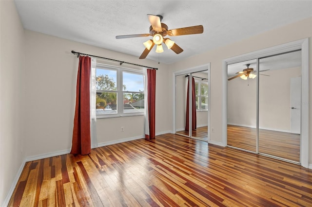 unfurnished bedroom with hardwood / wood-style flooring, ceiling fan, two closets, and a textured ceiling