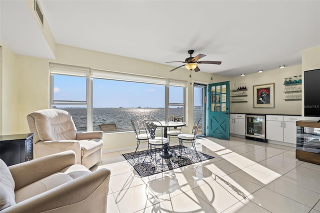 living room with beverage cooler, light tile patterned floors, ceiling fan, a water view, and bar area