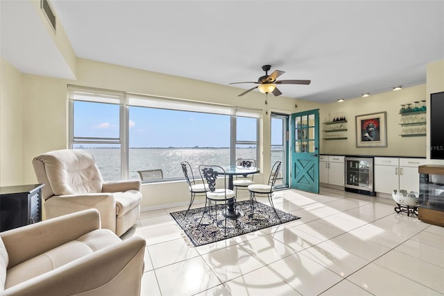 living room with light tile patterned flooring, a water view, wine cooler, and ceiling fan