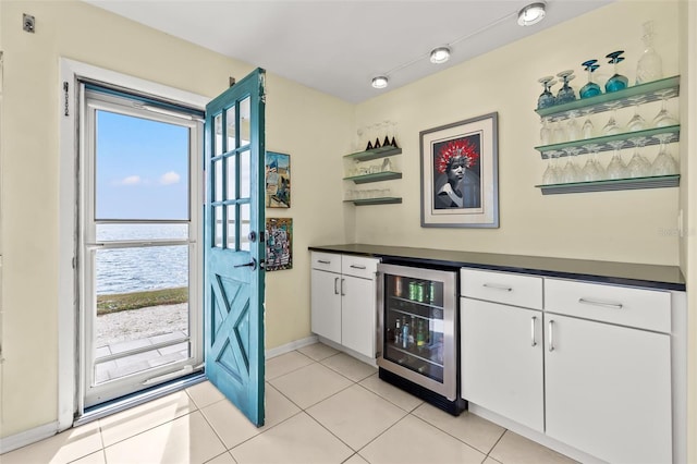 bar with a water view, white cabinetry, beverage cooler, and light tile patterned flooring