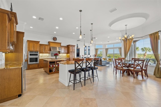 kitchen featuring pendant lighting, a spacious island, light stone counters, decorative backsplash, and exhaust hood