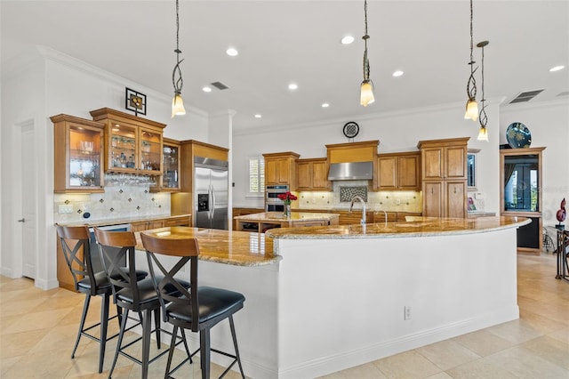 kitchen with a large island with sink, stainless steel built in refrigerator, pendant lighting, and wall chimney range hood