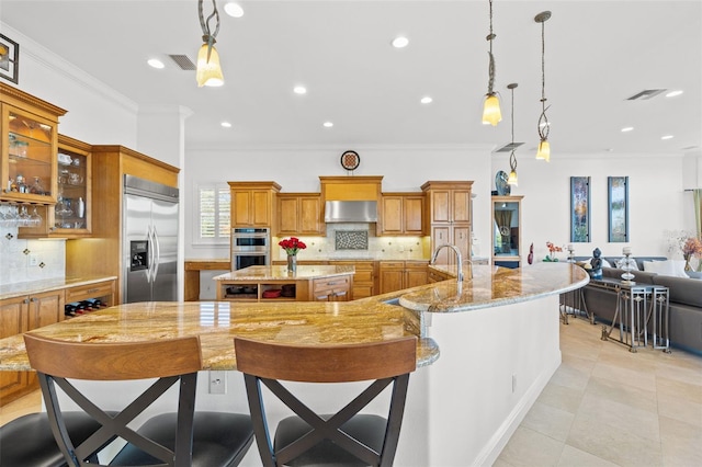 kitchen featuring a kitchen breakfast bar, hanging light fixtures, ornamental molding, a large island with sink, and stainless steel appliances