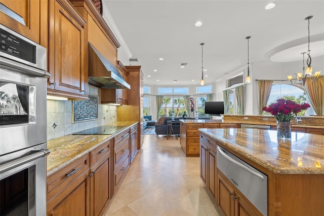 kitchen with a large island, hanging light fixtures, stainless steel appliances, light stone countertops, and wall chimney exhaust hood