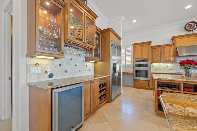 kitchen featuring ornamental molding, stainless steel appliances, beverage cooler, light stone countertops, and exhaust hood