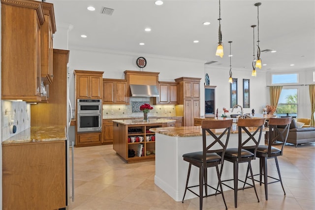 kitchen with extractor fan, pendant lighting, a kitchen breakfast bar, a kitchen island with sink, and stainless steel double oven