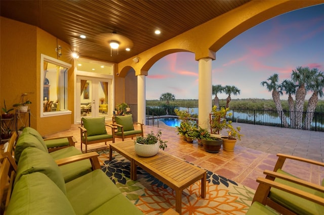 patio terrace at dusk with an outdoor living space, a water view, and a fenced in pool