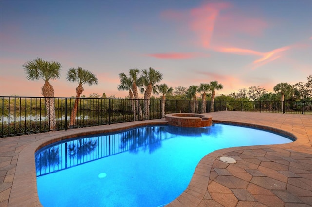 pool at dusk with an in ground hot tub and a patio