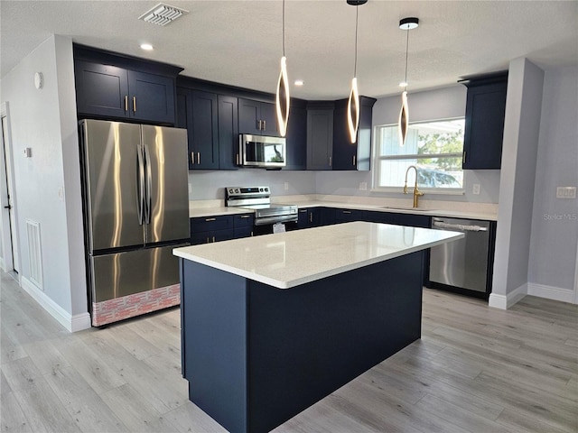 kitchen with sink, stainless steel appliances, a center island, light stone counters, and decorative light fixtures