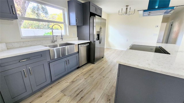 kitchen with light stone counters, stainless steel appliances, sink, and light hardwood / wood-style flooring