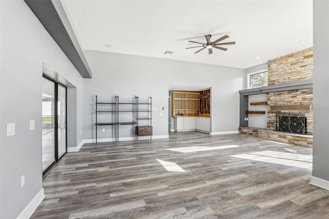 unfurnished living room featuring hardwood / wood-style flooring, ceiling fan, and a stone fireplace