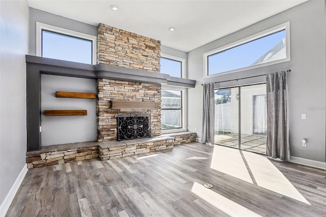 unfurnished living room with a stone fireplace, a towering ceiling, and hardwood / wood-style floors